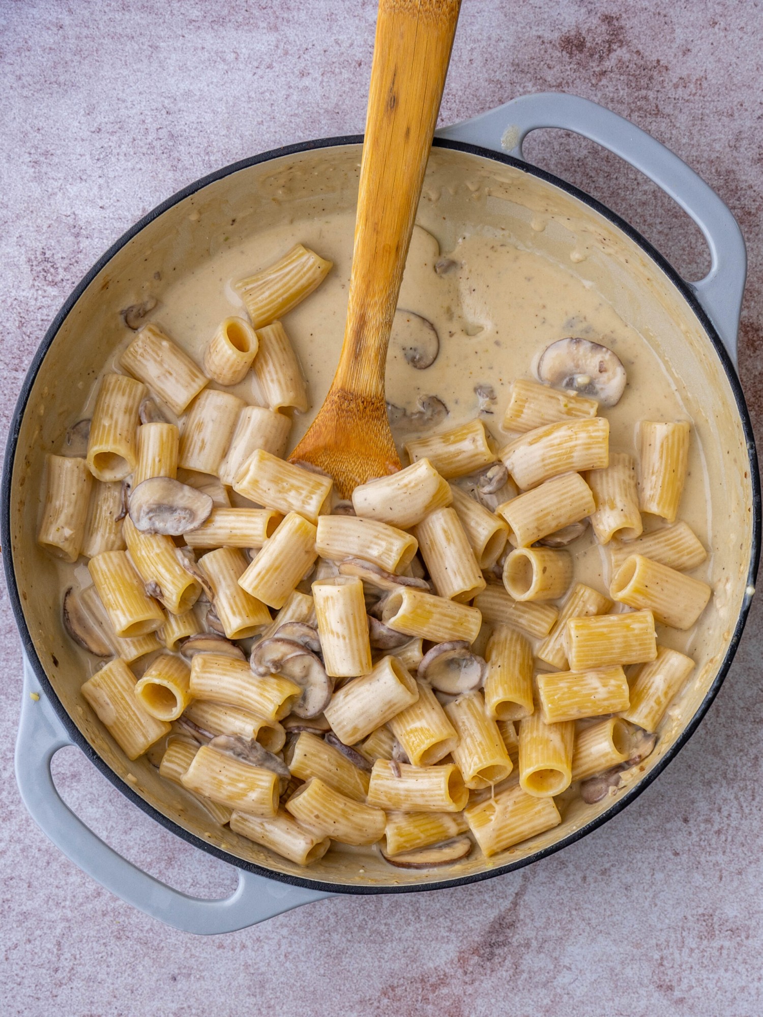 Above view of mushroom alfredo pasta in a pan with a wooden spoon