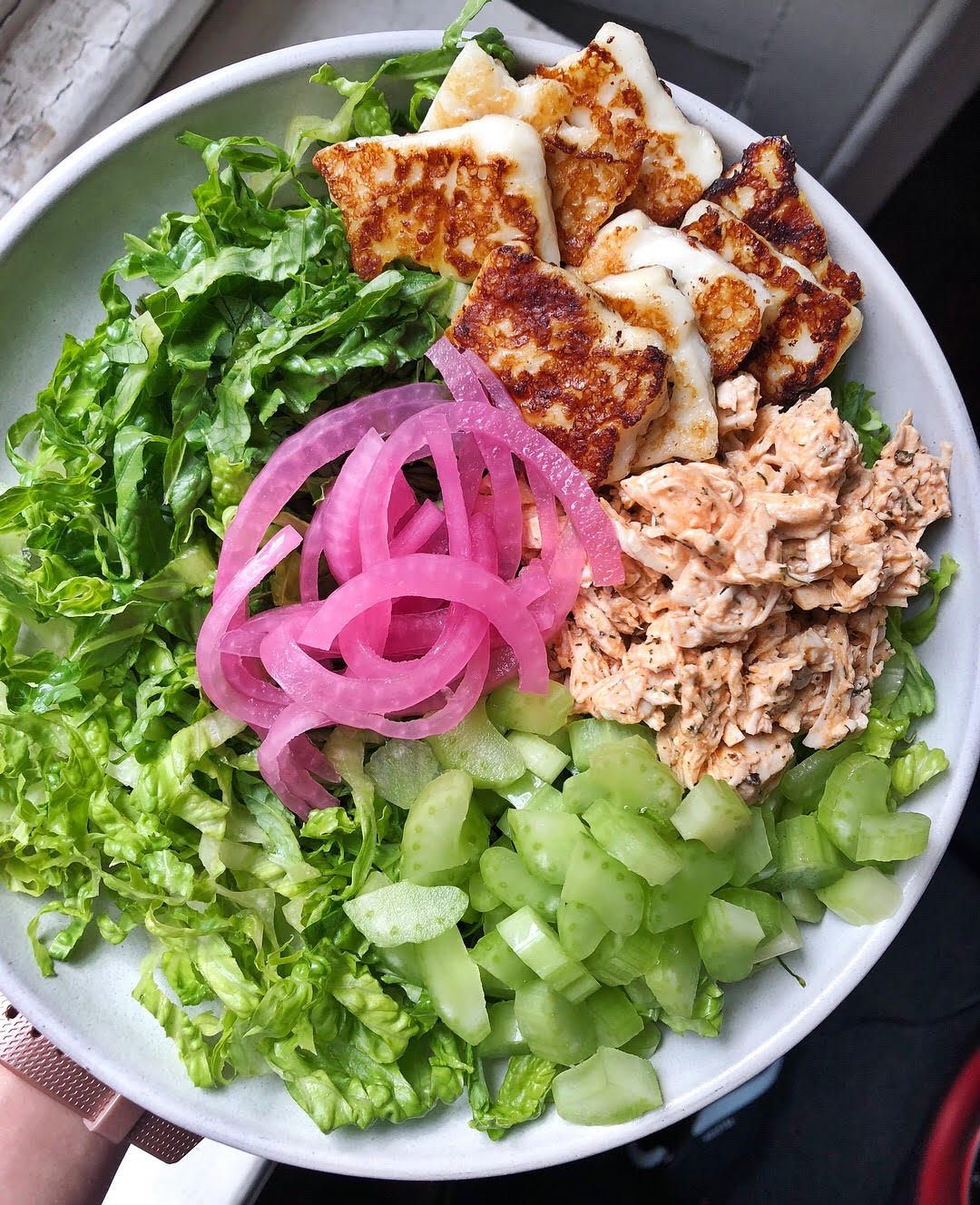 Above view of a salad with romaine lettuce, pickled red onions, halloumi cheese and shredded buffalo chicken