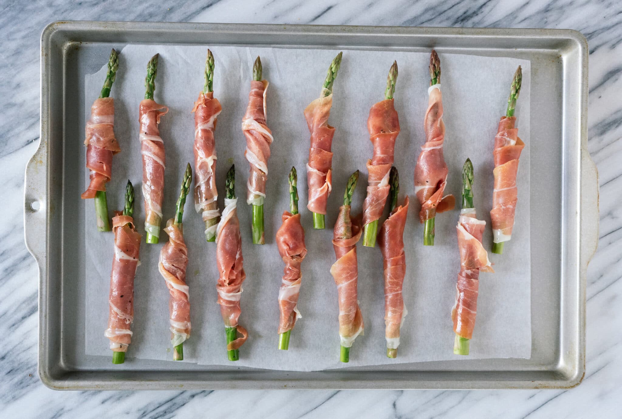 Above view of prosciutto wrapped asparagus on a baking sheet prior to being baked