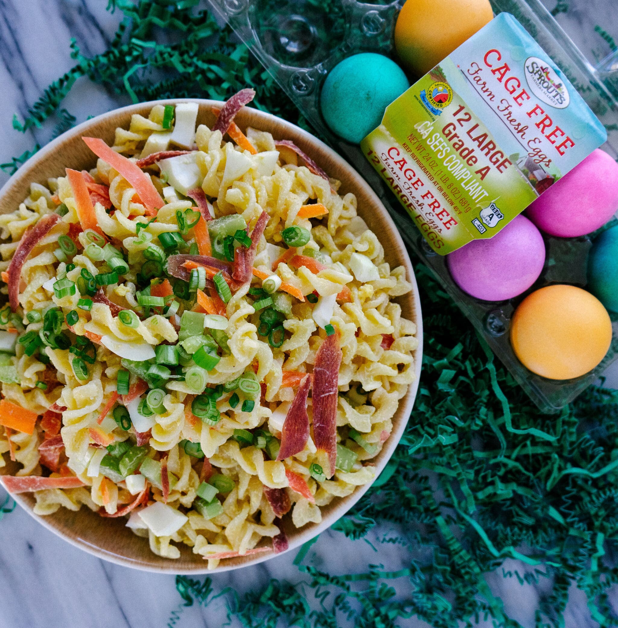Above view of deviled egg pasta salad in a bowl with dyed Easter eggs on the side