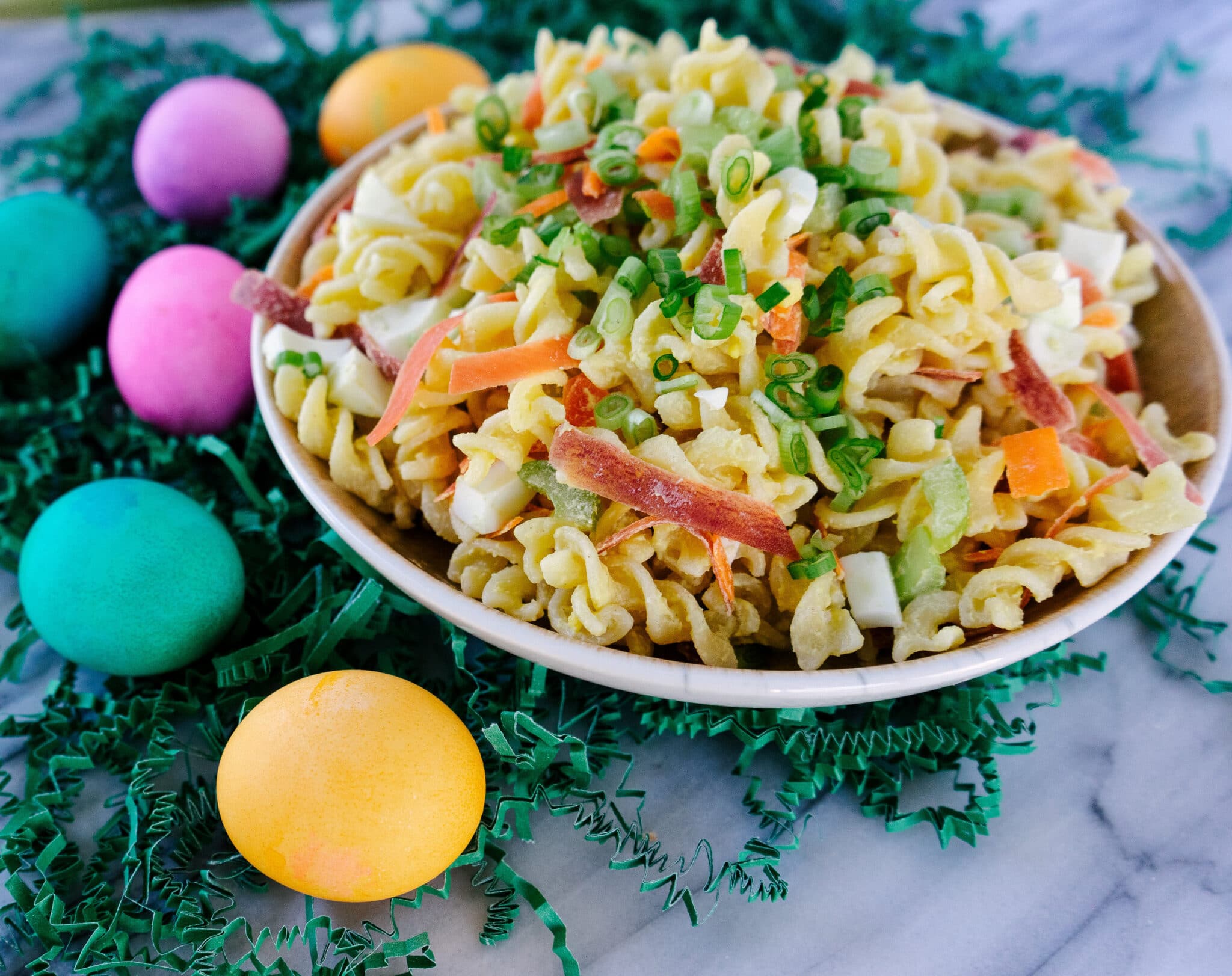 Three quarter view of deviled egg pasta salad in a bowl with colorful Easter eggs on the side