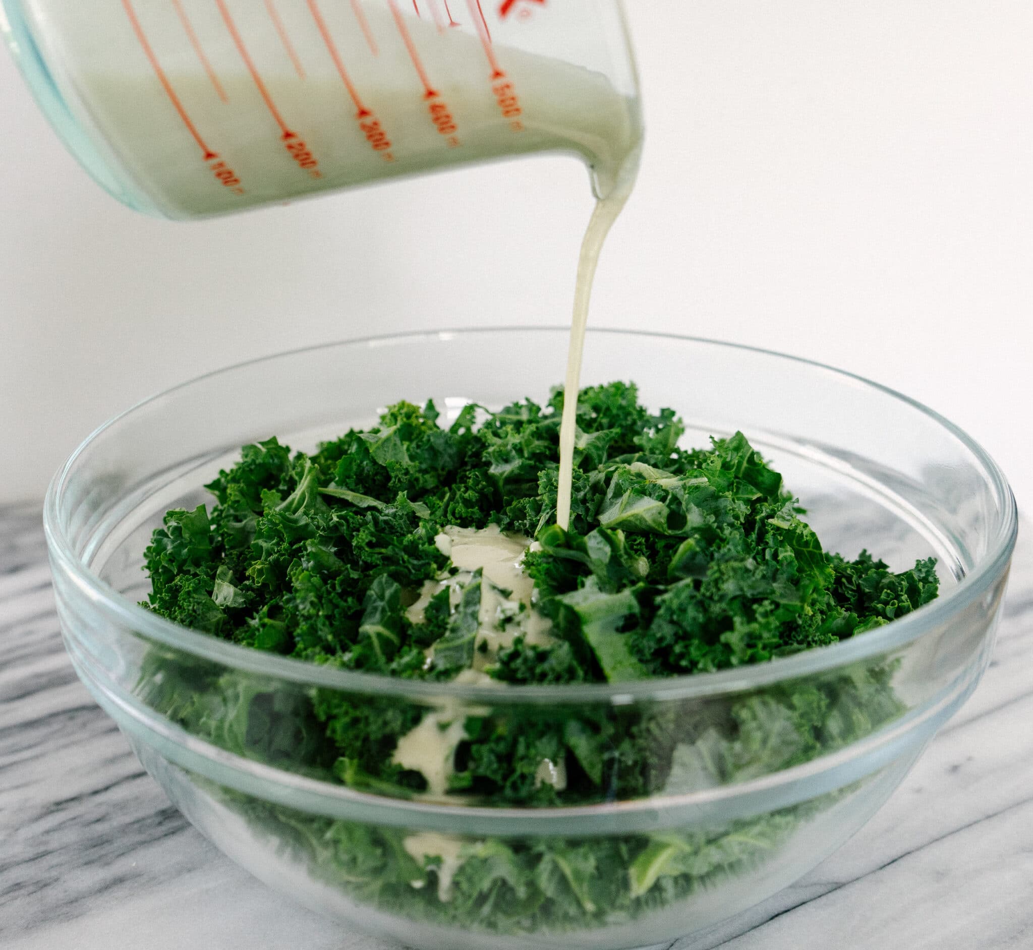 Side view of creamy cashew dressing pouring onto a bowl of chopped kale