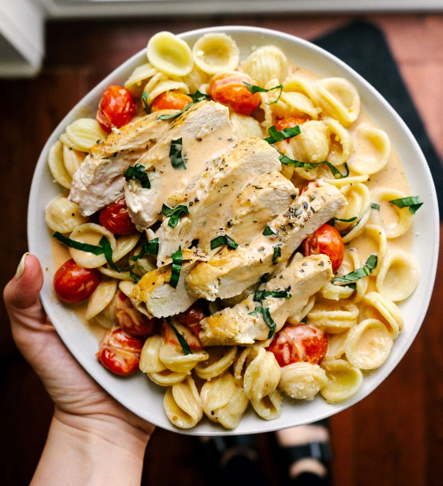 Above view of sliced tomato basil chicken with pasta on a serving plate