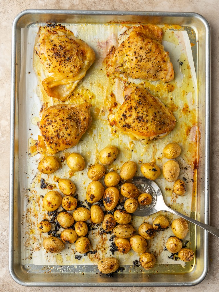 Above view of baked chicken thighs and roasted potatoes on a baking sheet