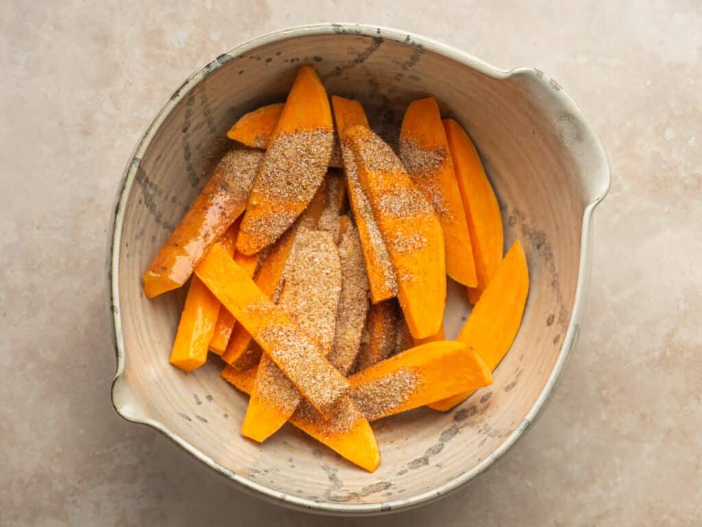 Sweet potato wedges in a bowl with oil and a seasoning blend on them