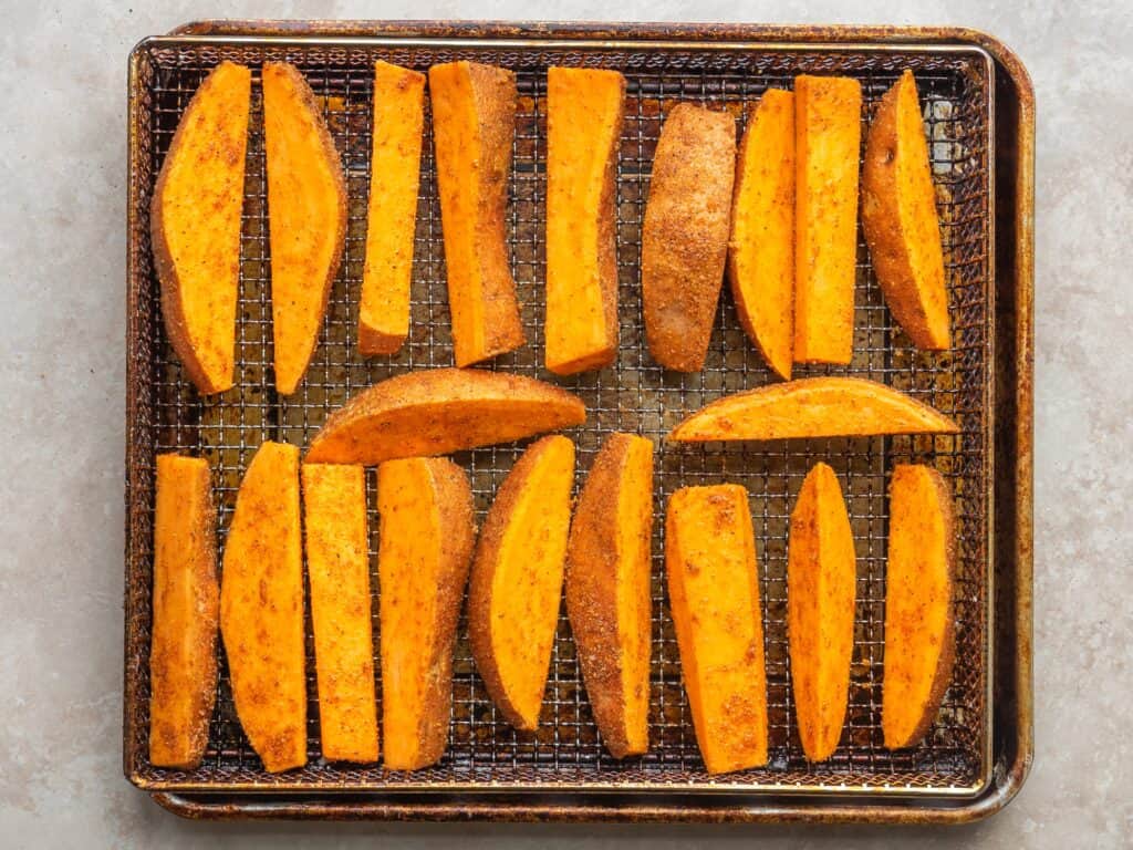 seasoning sweet potato wedges arranged on an air fryer tray