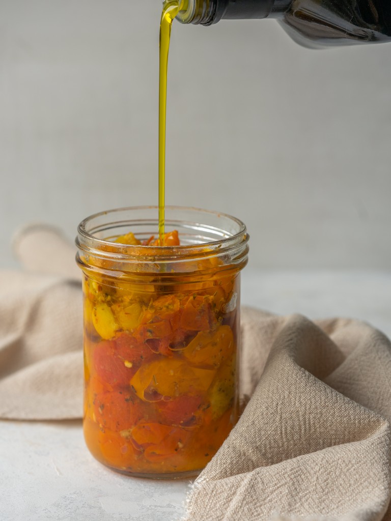 Marinated cherry tomatoes in a jar with olive oil pouring on top of them