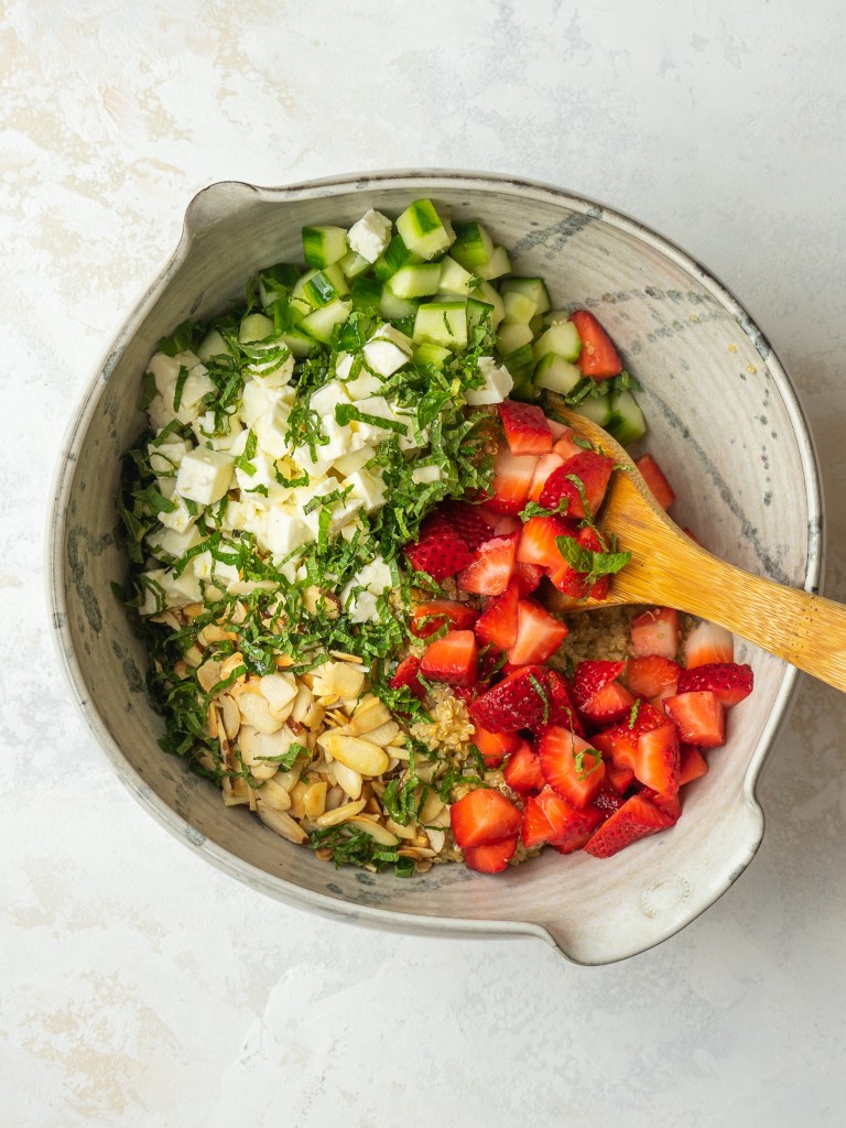 Above view of a wooden mixing spoon in a bowl with ingredients for the strawberry feta salad