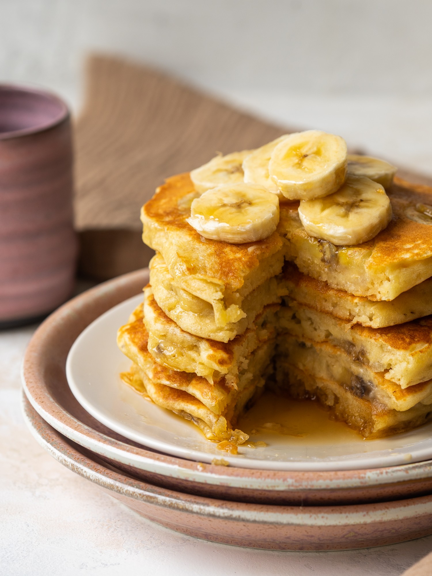 Side view of fluffy banana pancakes stacked up on a plated with a triangle cut out of the pancakes
