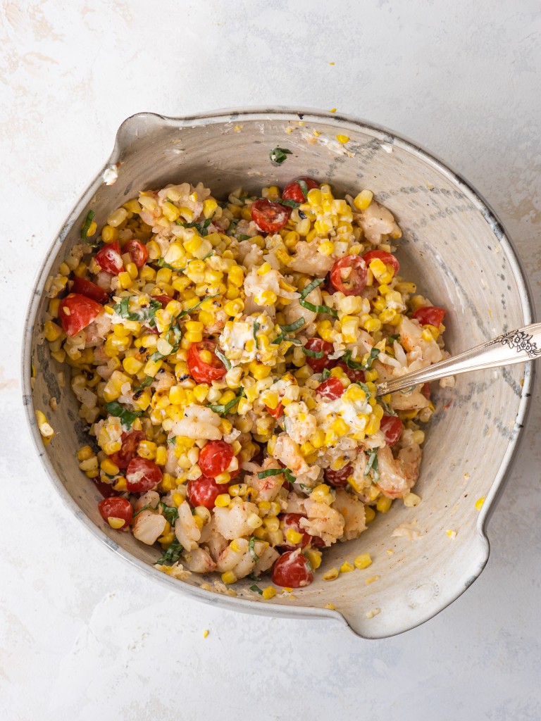 Creamy grilled corn salad with shrimp and tomatoes in a mixing bowl