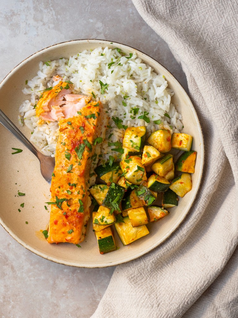 Above view of a serving of harissa salmon with a bite out of it with roasted zucchini and rice