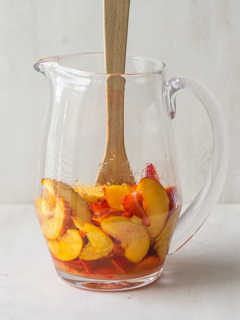 Side view of strawberries, peaches and a wooden mixing spoon in a pitcher