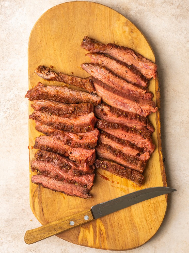Sliced air fryer flank steak on a cutting board with a sharp knife