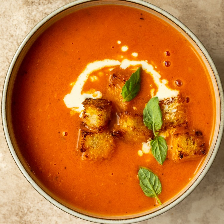 Above view of tomato soup in a serving bowl with cream and crouton garnishes