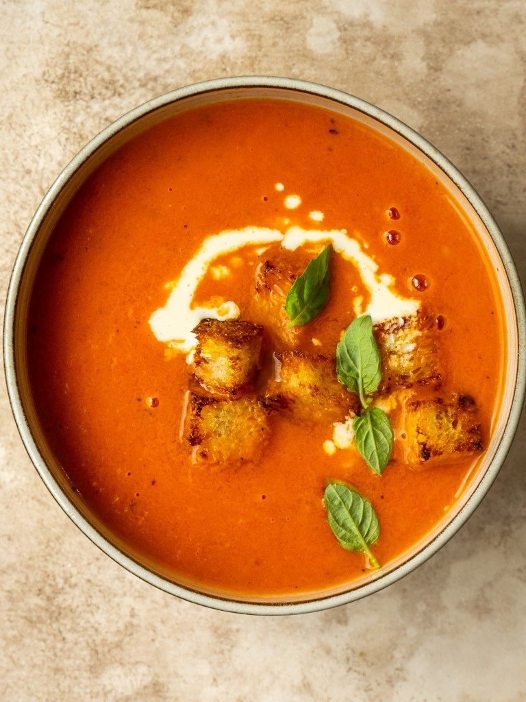 Above view of tomato soup in a serving bowl with cream and crouton garnishes