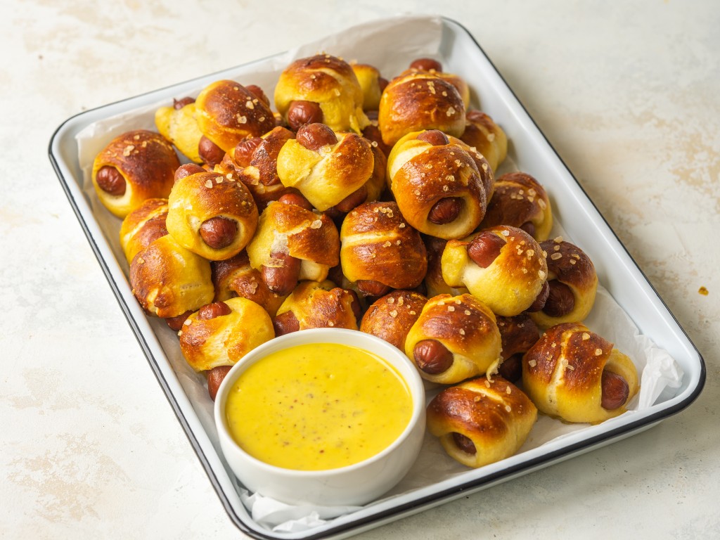 Three quarter view of mini pretzel dogs on a serving platter with mustard