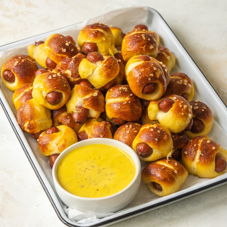 Three quarter view of mini pretzel dogs on a serving platter with mustard