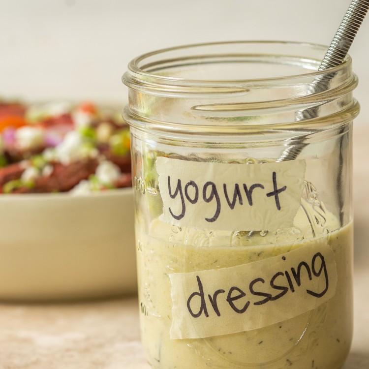 Jar of healthy salad dressing in a jar with a whisk in it in front of a salad