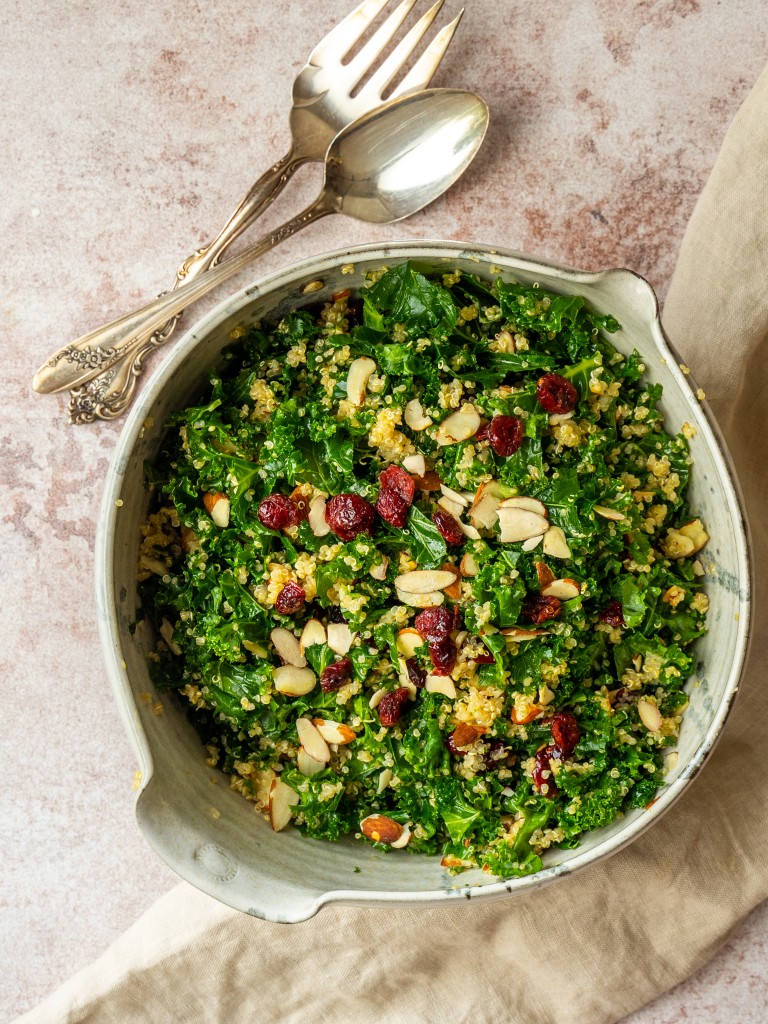 Above view of kale and quinoa salad in a mixing bowl with serving utensils next to it