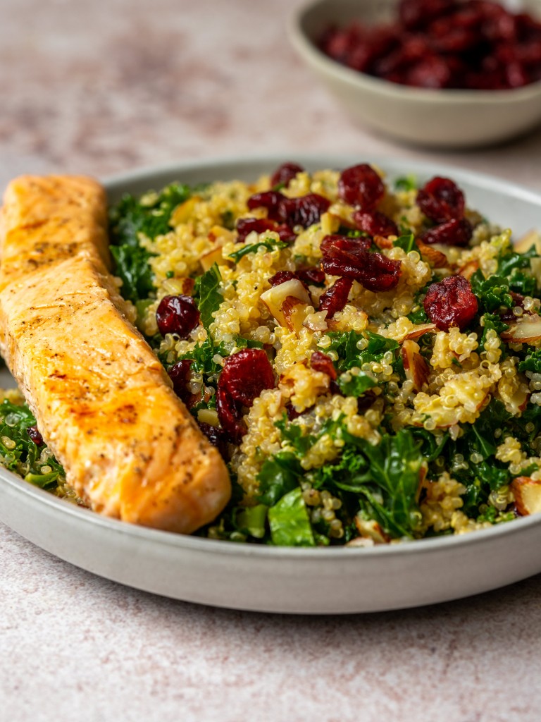 Three quarter view of a kale salad with cranberries and filet of salmon