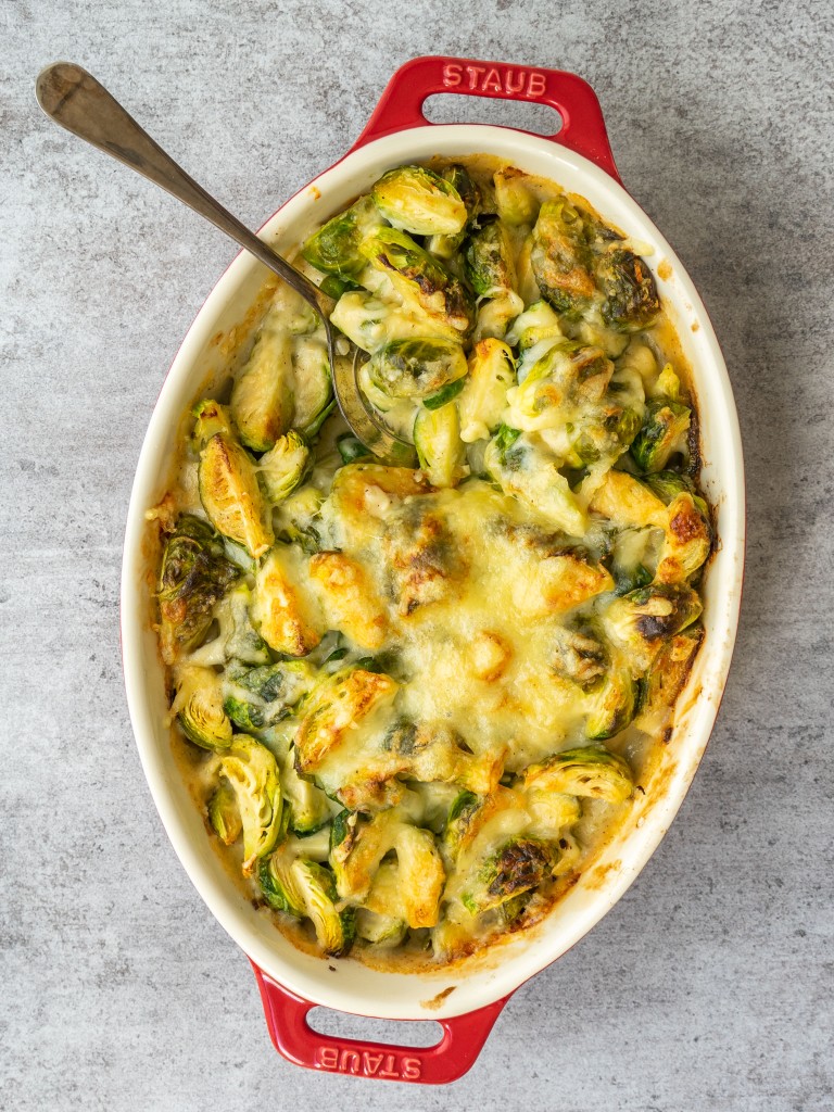 Above view of brussles sprouts with cheese in a casserole dish with a serving spoon in it