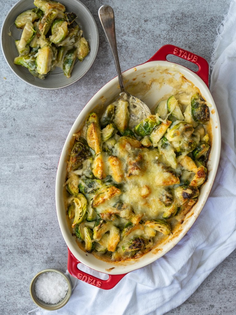 Cheesy brussels sprouts in a small serving place next to a casserole dish