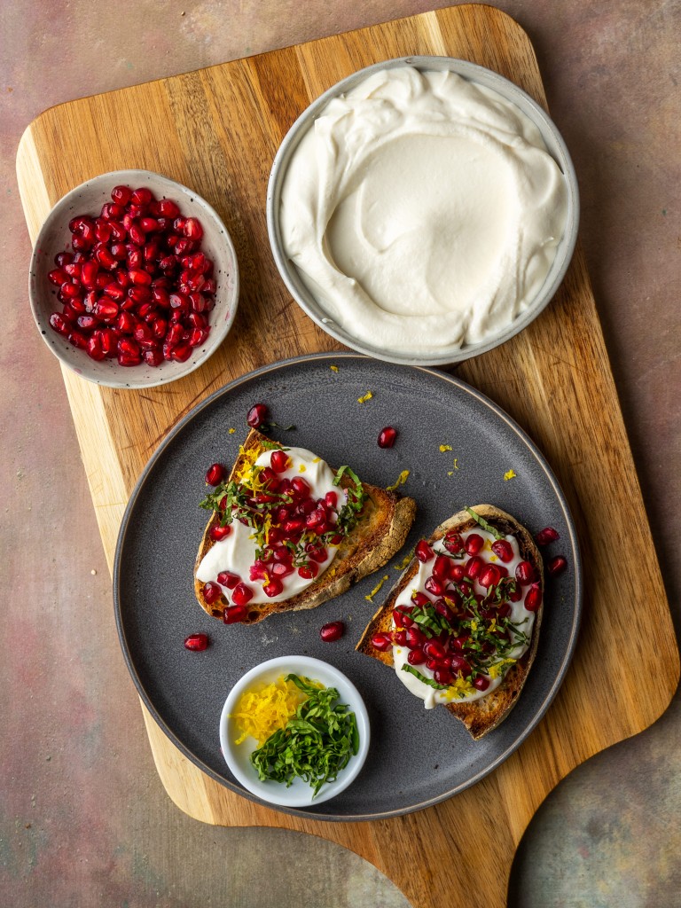 whipped ricotta toast topped with pomegranate seeds, lemon zest and basil