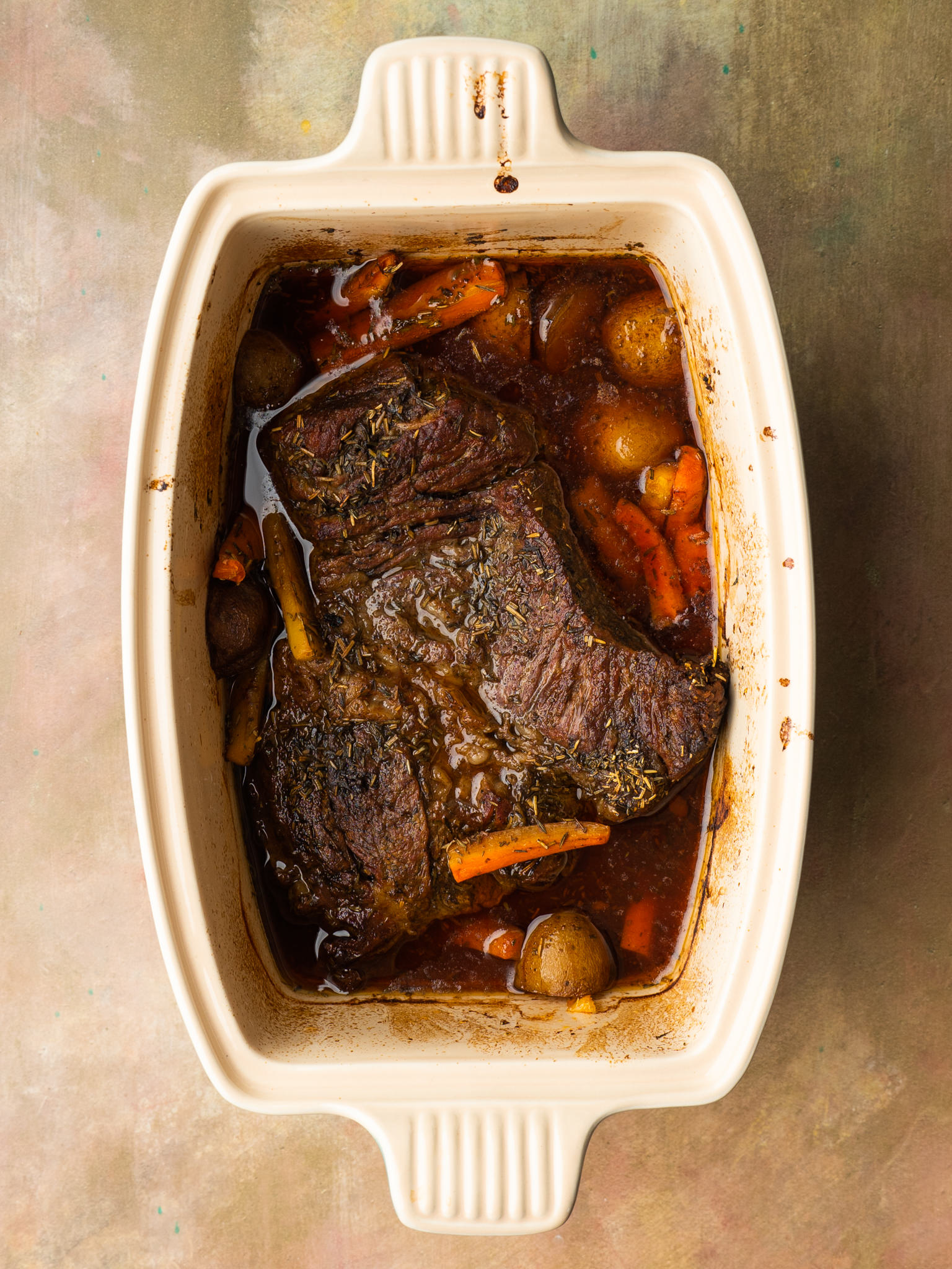 Above view of chuck roast, potatoes, and carrots in a roasting pan
