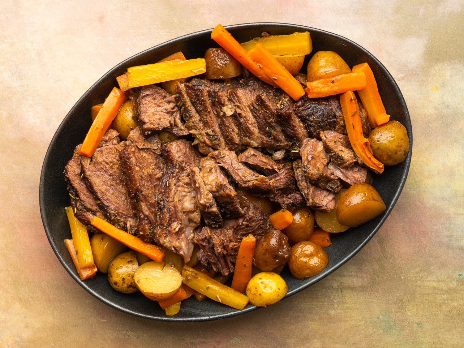 Sliced tender chuck roast on a serving tray with carrots and potatoes