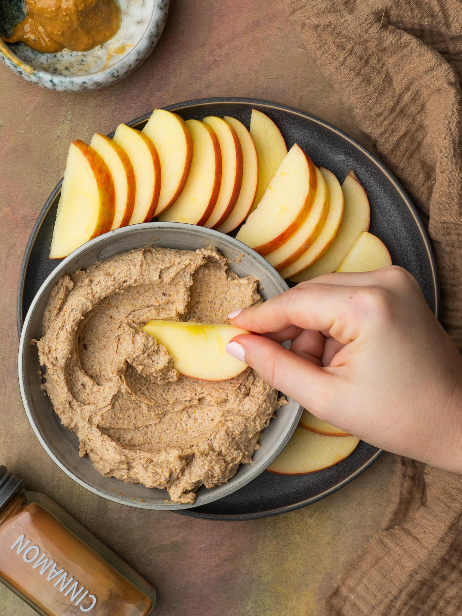 Above view of a hand holding an apple dipping into a peanut butter dip
