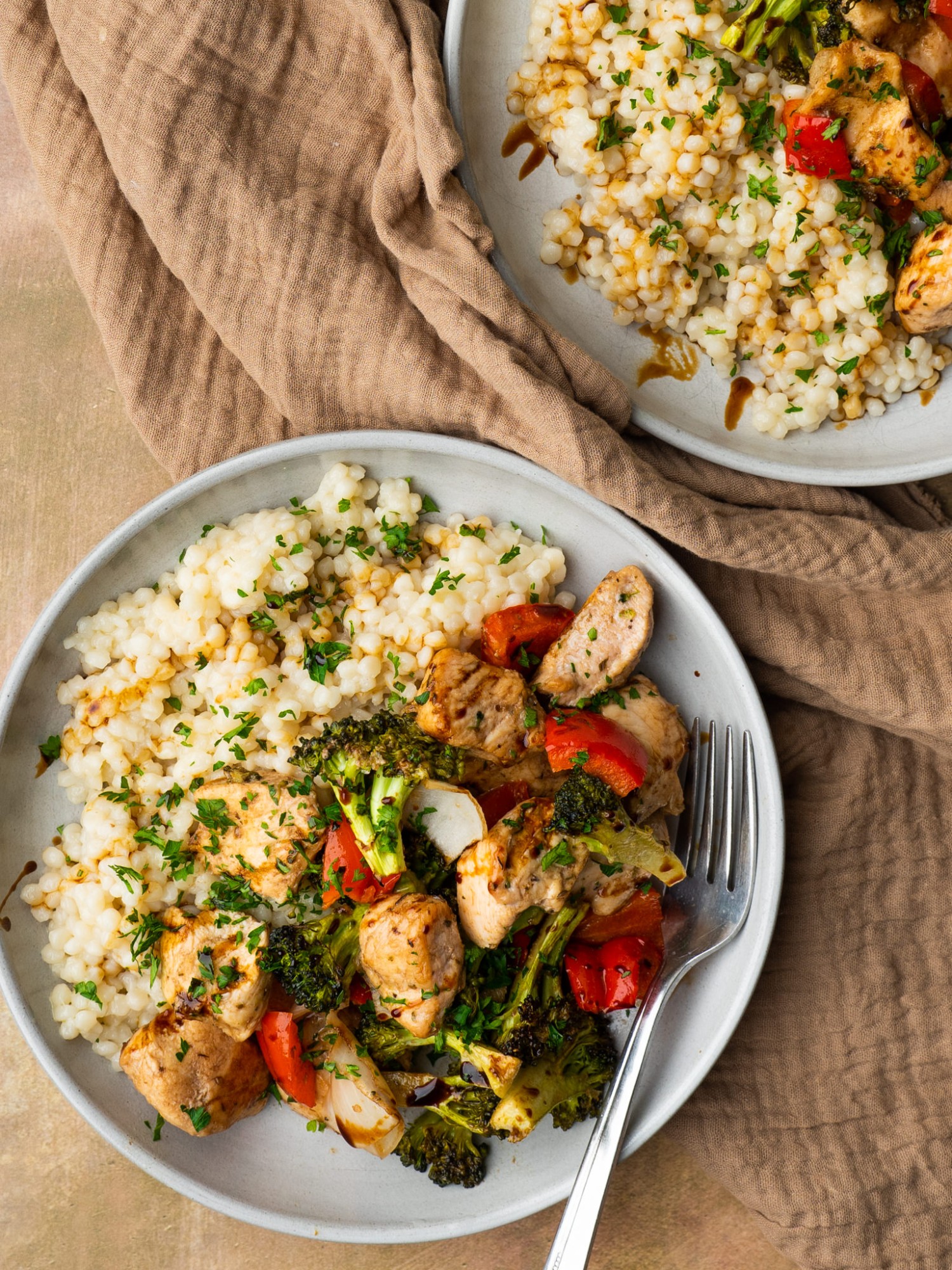 Above view of baked honey balsamic chicken and veggies on a serving plate with pearl couscous