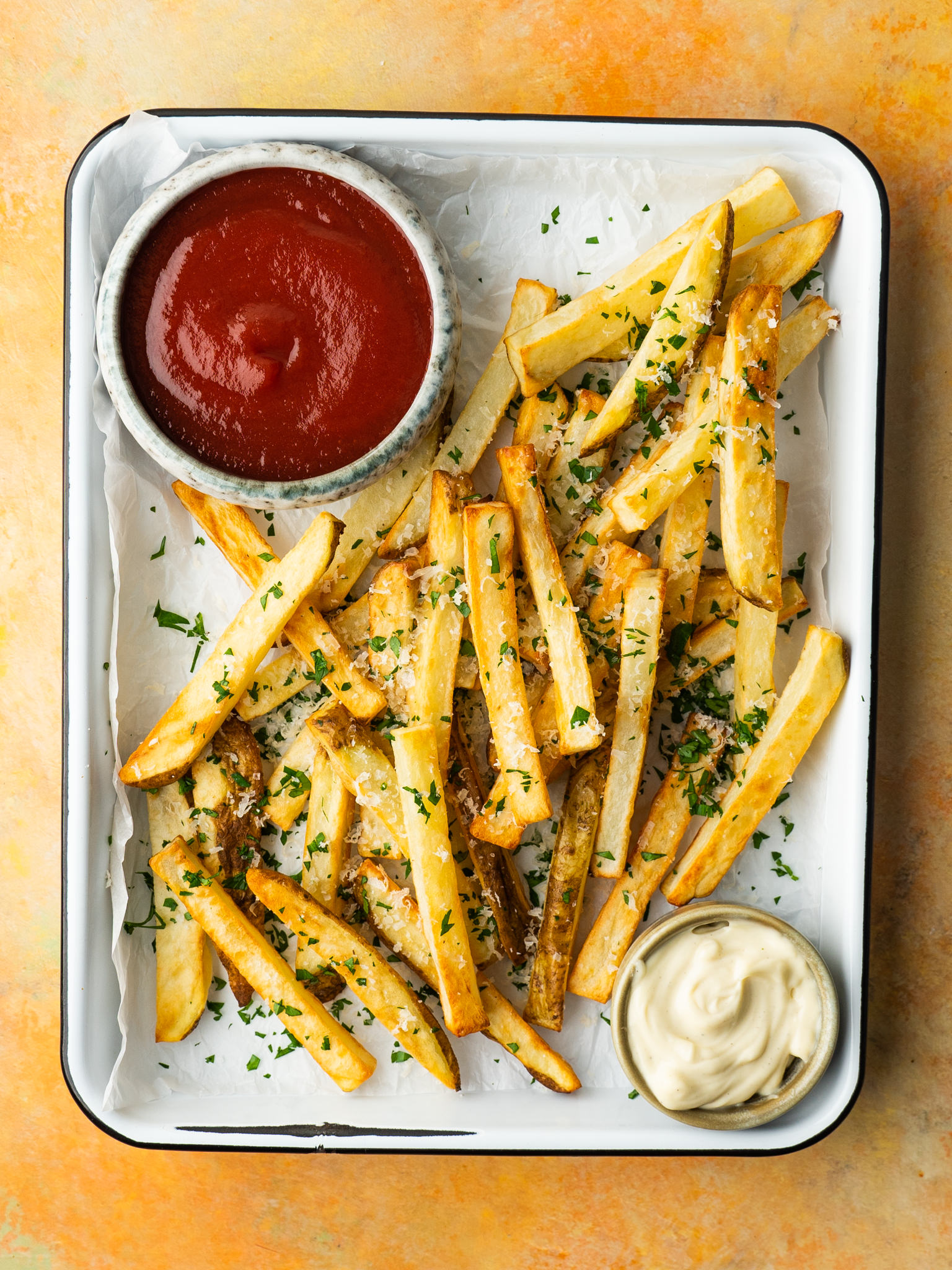 Above view of air fryer french fries served with parmesan cheese, fresh herbs and dipping sauces