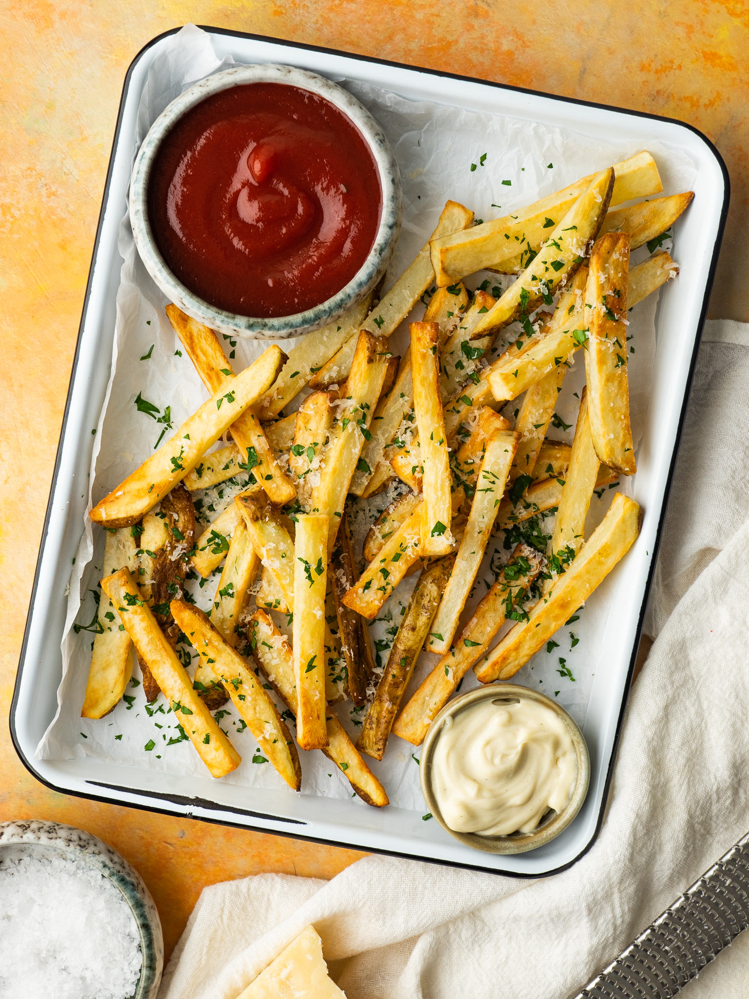 Above view of air fryer french fries served with parmesan cheese, fresh herbs and dipping sauces