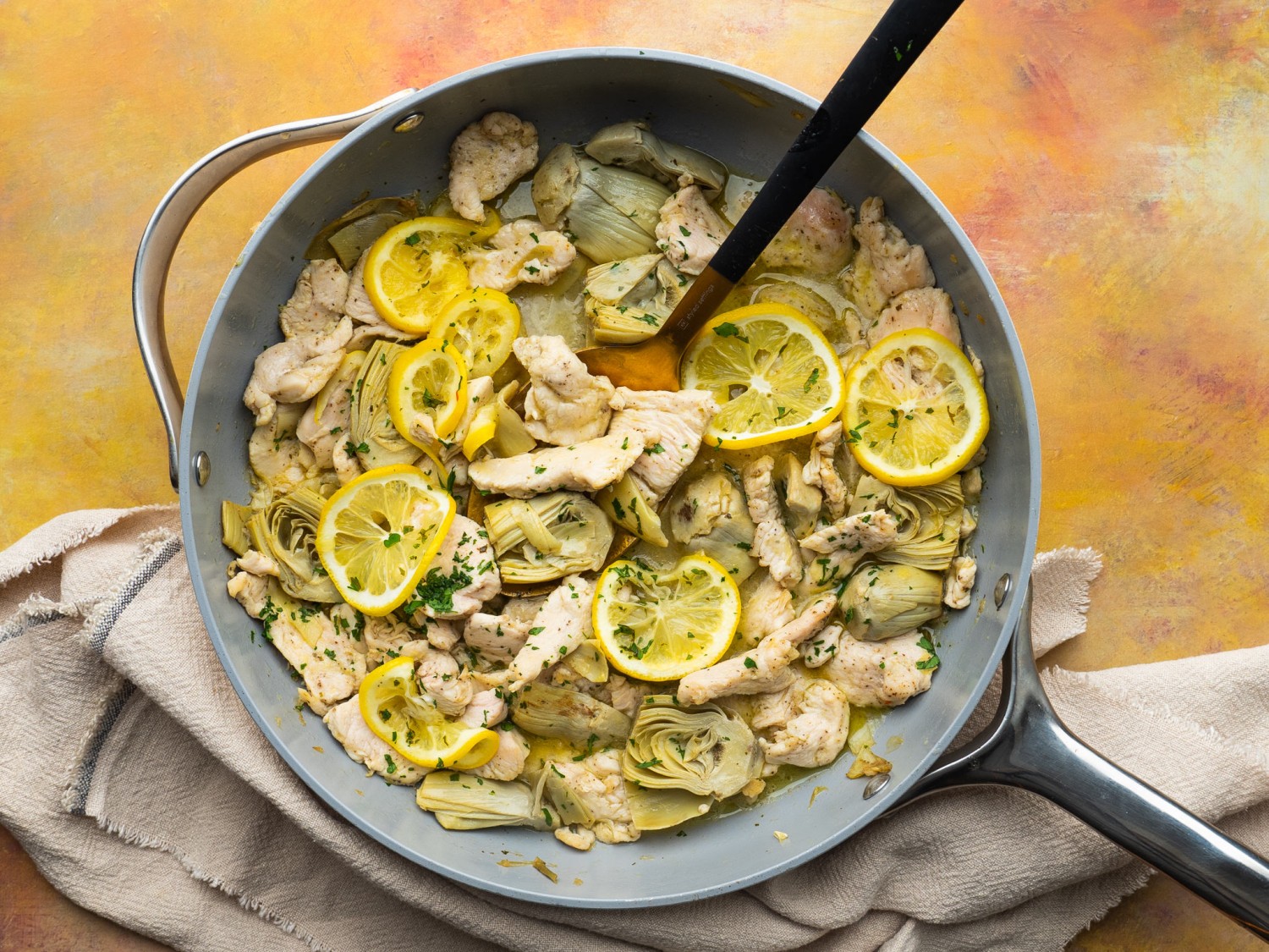 Chicken with artichokes and lemon in a pan with a serving spoon