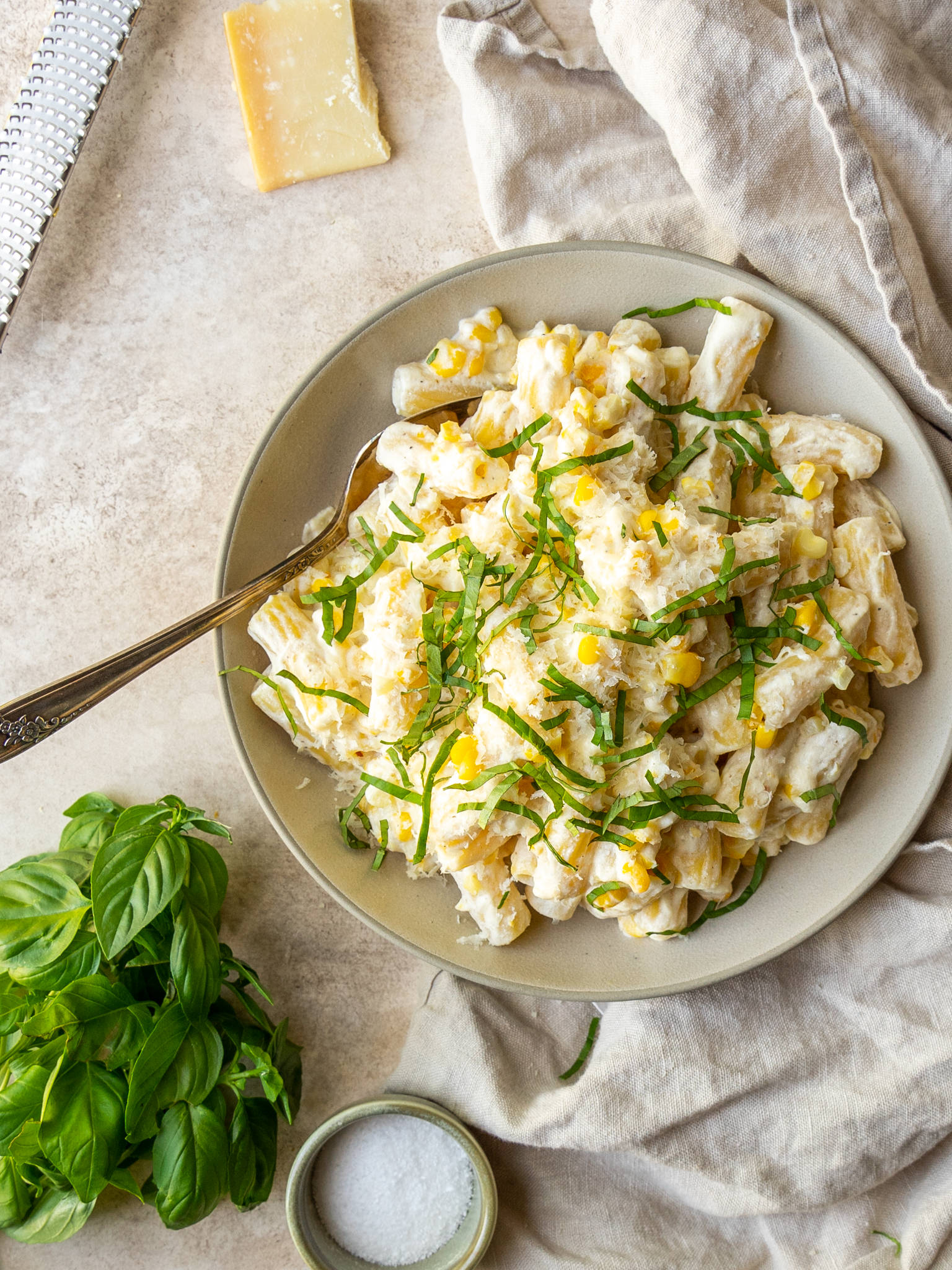 Creamy corn pasta recipe with basil on top in a serving bowl with a serving spoon