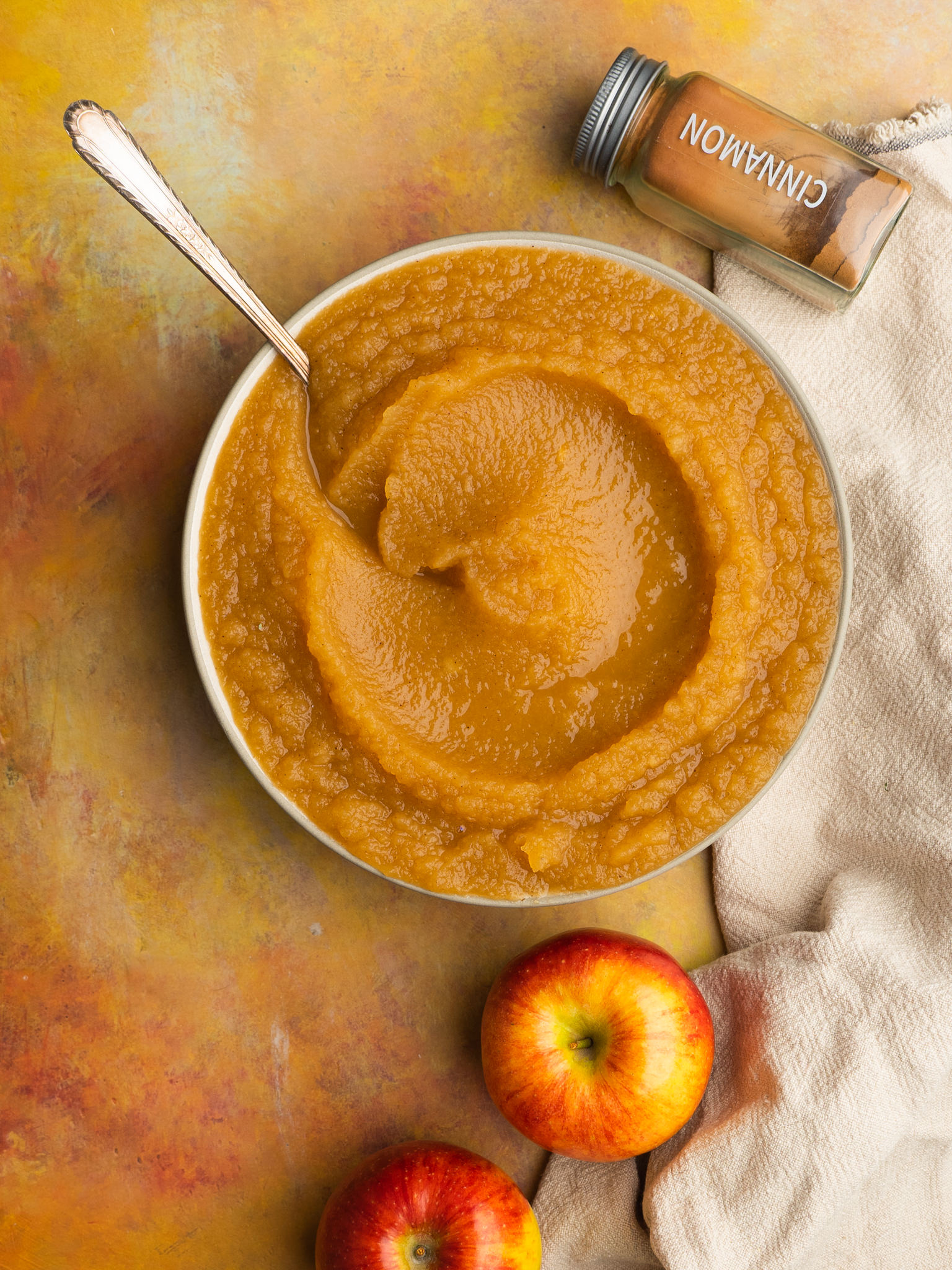 Crockpot applesauce in a serving bowl with an apple and cinnamon next to it