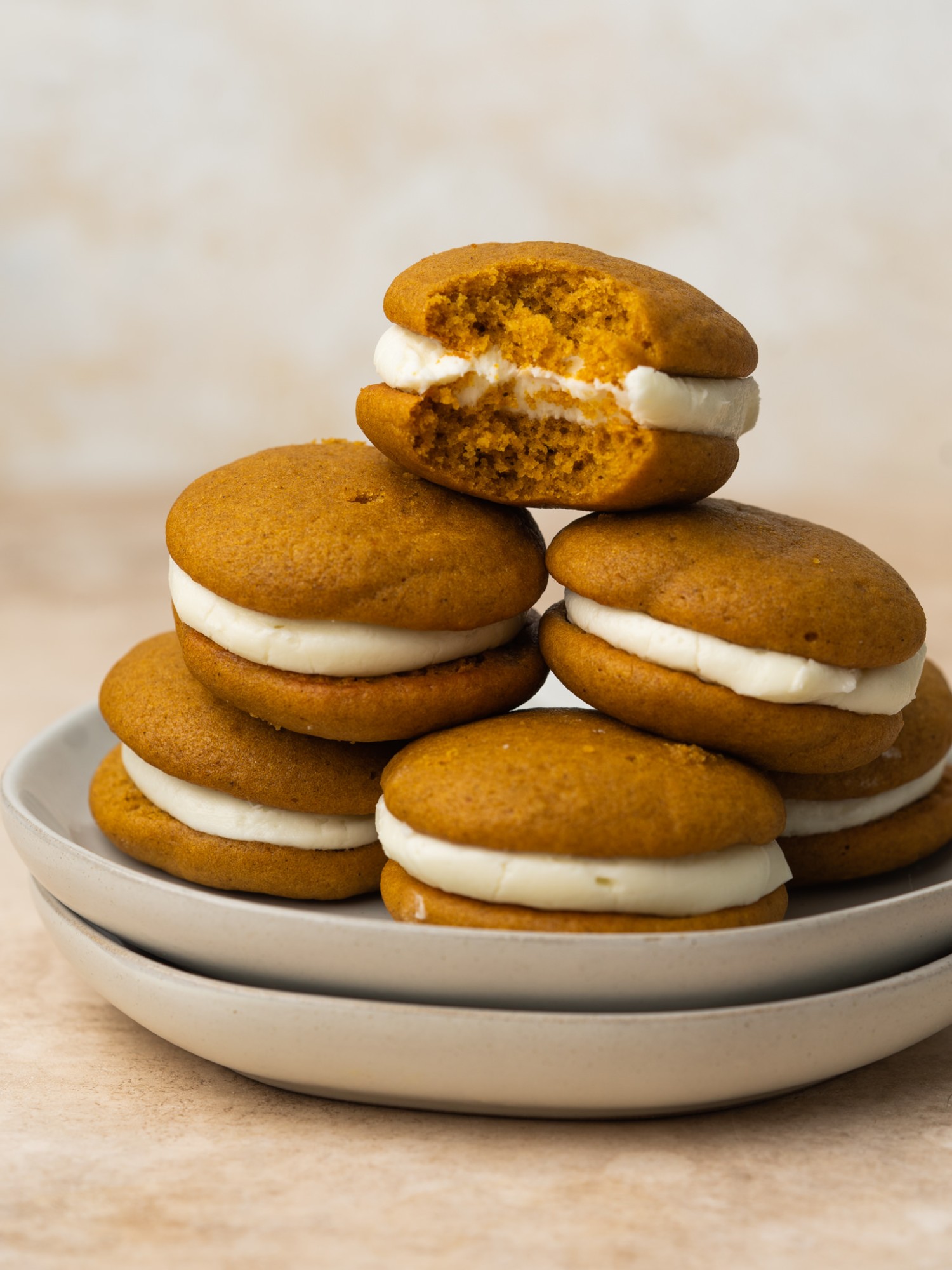 pumpkin whoopie pies stacked up on a plate with a bite out of the top one