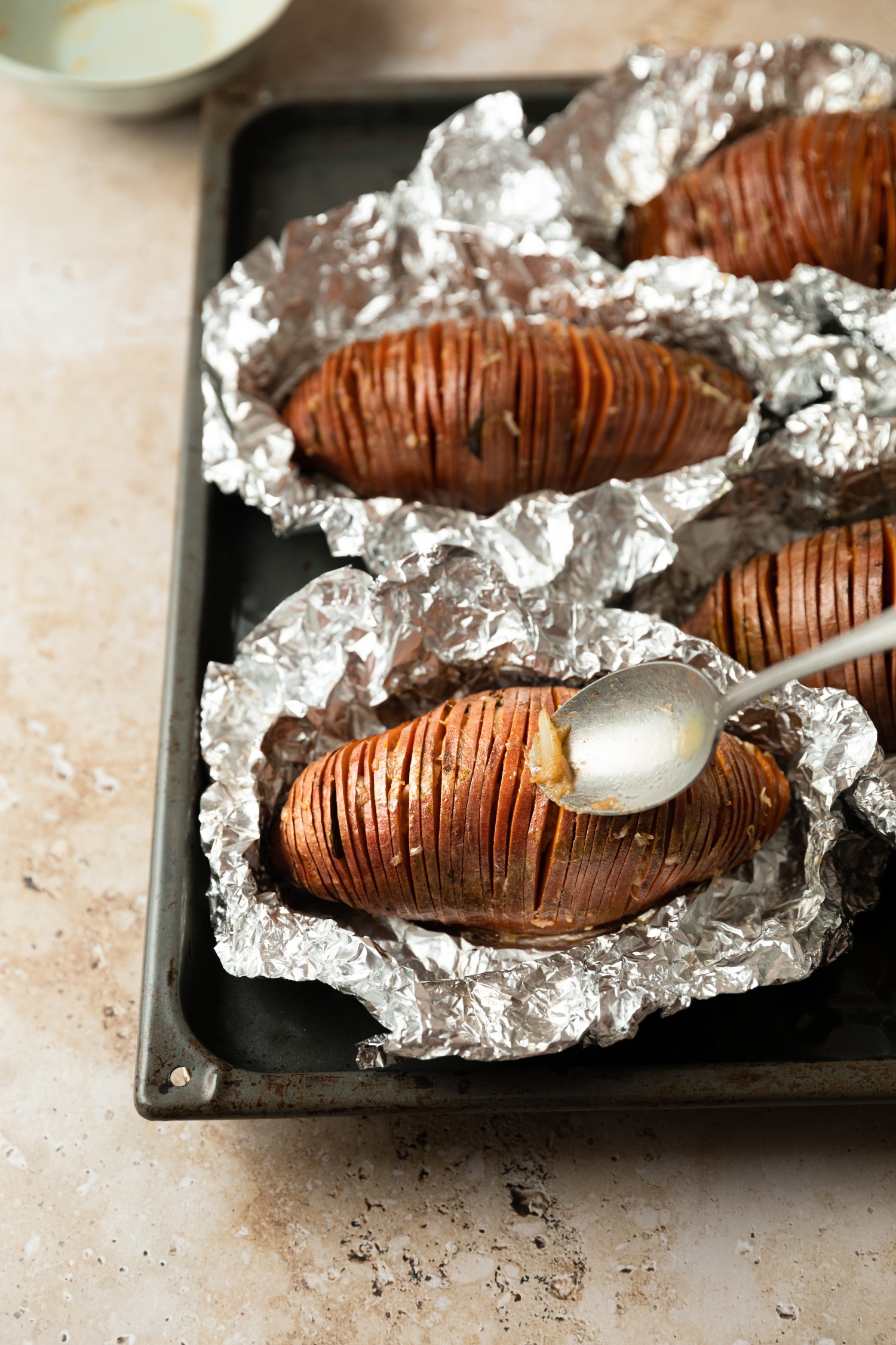 Garlic butter being poured into hasselback sweet potatoes