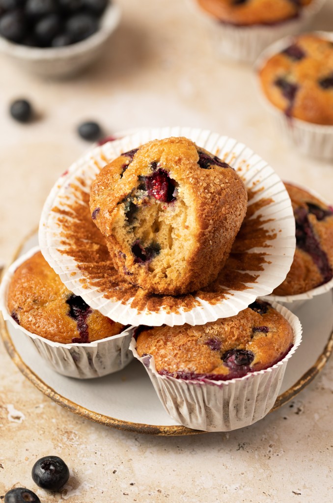 Blueberry yogurt muffins on a serving platter with a bite out of it one of the muffins