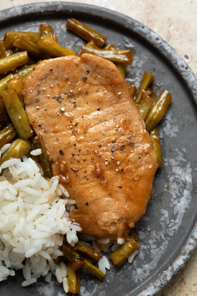Close up above view of a honey garlic pork chop on a serving plate with green beans and rice