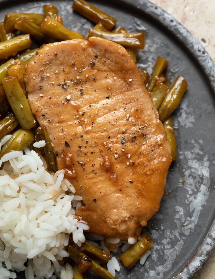 Close up above view of a honey garlic pork chop on a serving plate with green beans and rice