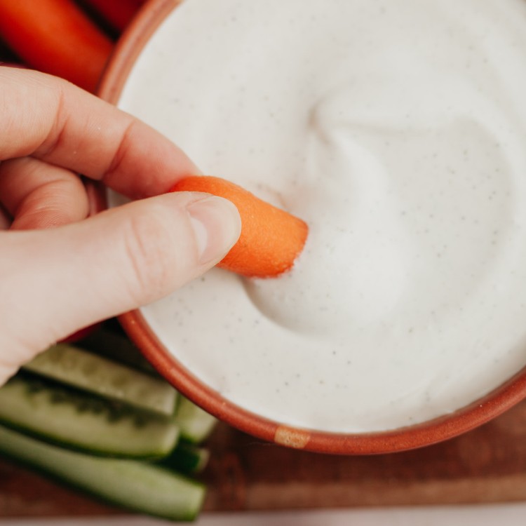 Above view of a carrot dipping into a bowl of whipped cottage cheese