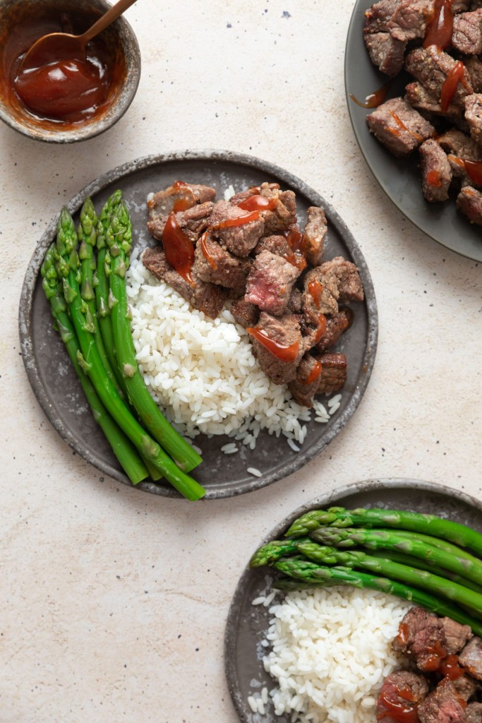 Steak bites made in the air fryer on a serving plate with rice and asparagus
