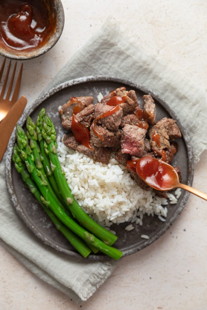 Steak bites made in the air fryer on a serving plate with rice and asparagus