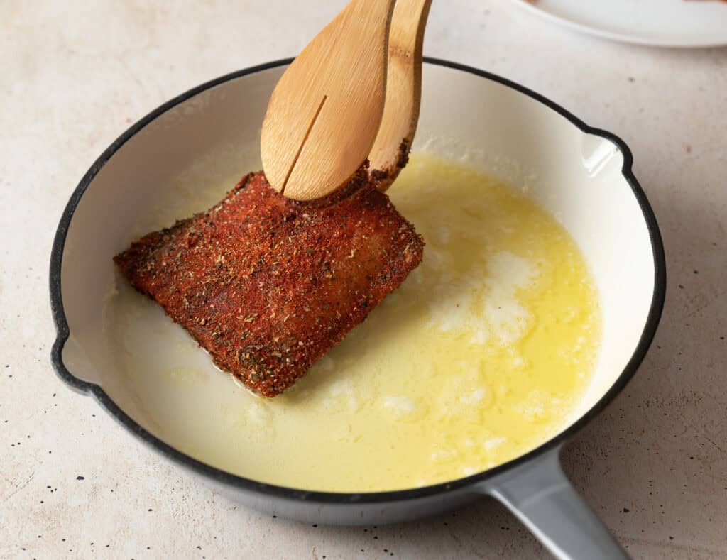 mahi mahi fillet being placed in a skillet with tongs
