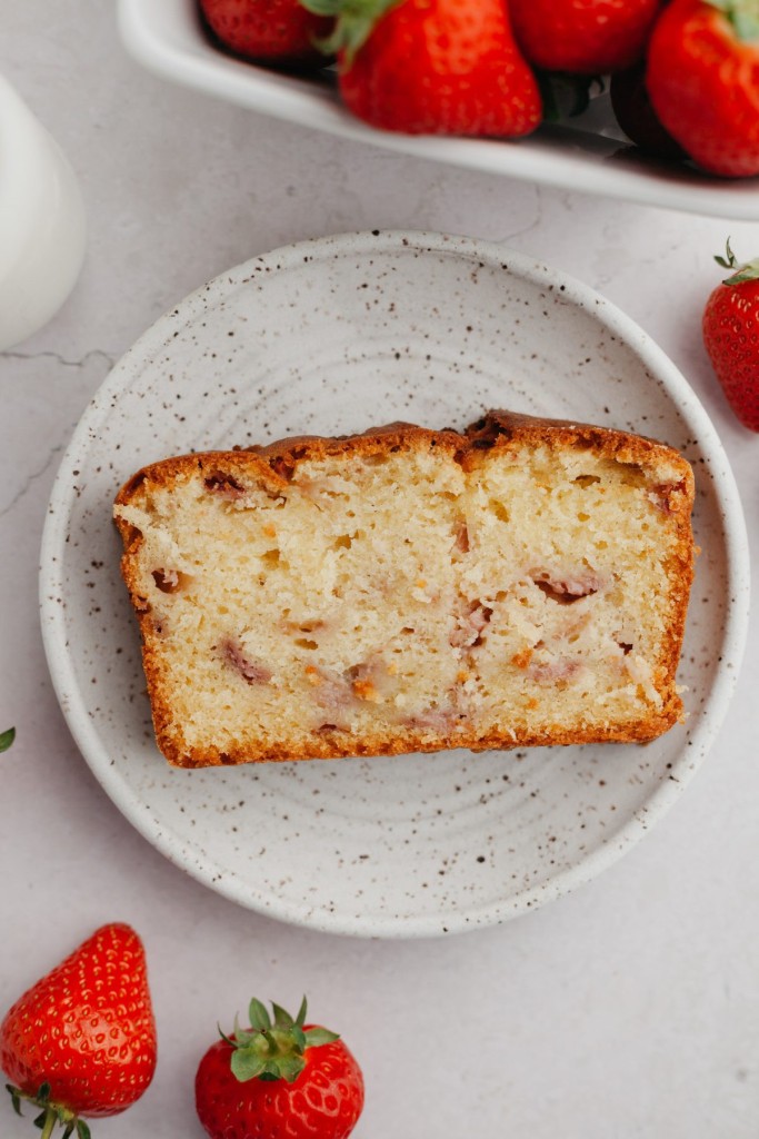 Slice of strawberry cake recipe on a serving plate with strawberries around it