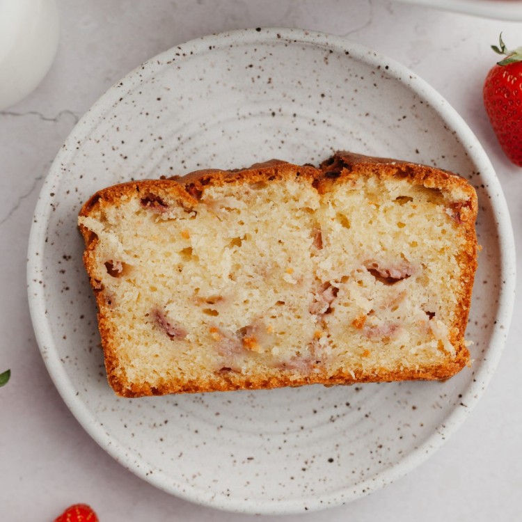 Slice of strawberry cake recipe on a serving plate with strawberries around it