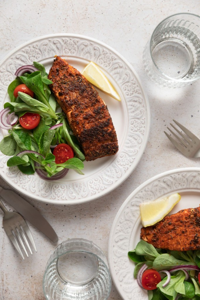 Above view of blackened salmon on a serving plate with a green salad and a wedge of lemon