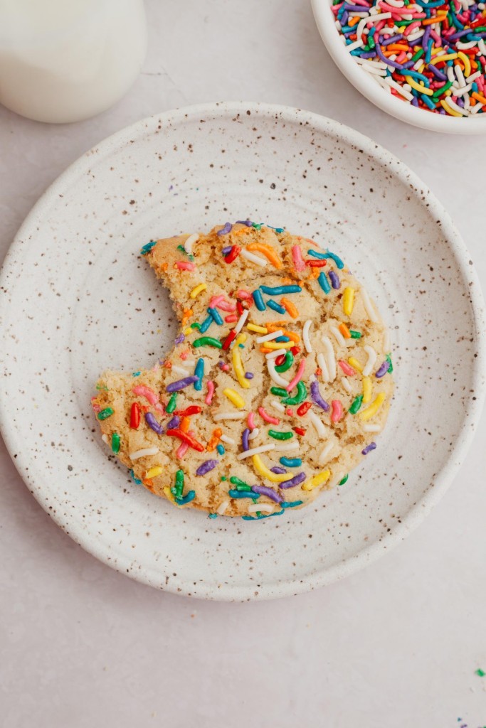 Above view of a sprinkle cookie on a plate with a bite taken out of it