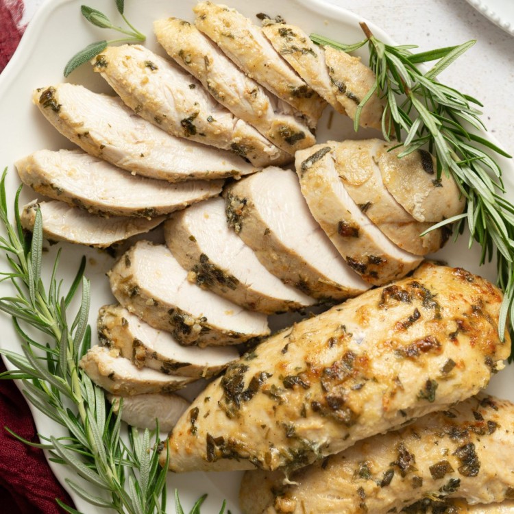 Sliced turkey tenderloin on a serving platter with fresh herbs